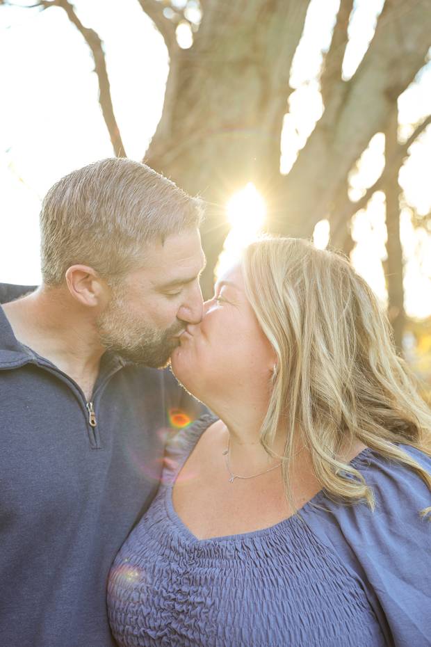 A couple kissing under a tree in late afternoon sun.