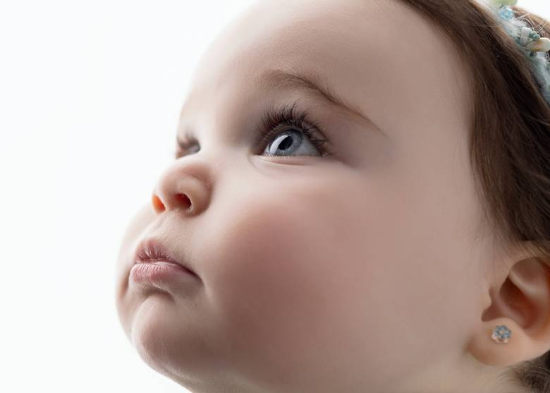 Close profile of a baby's face looking up, lit softly against white.
