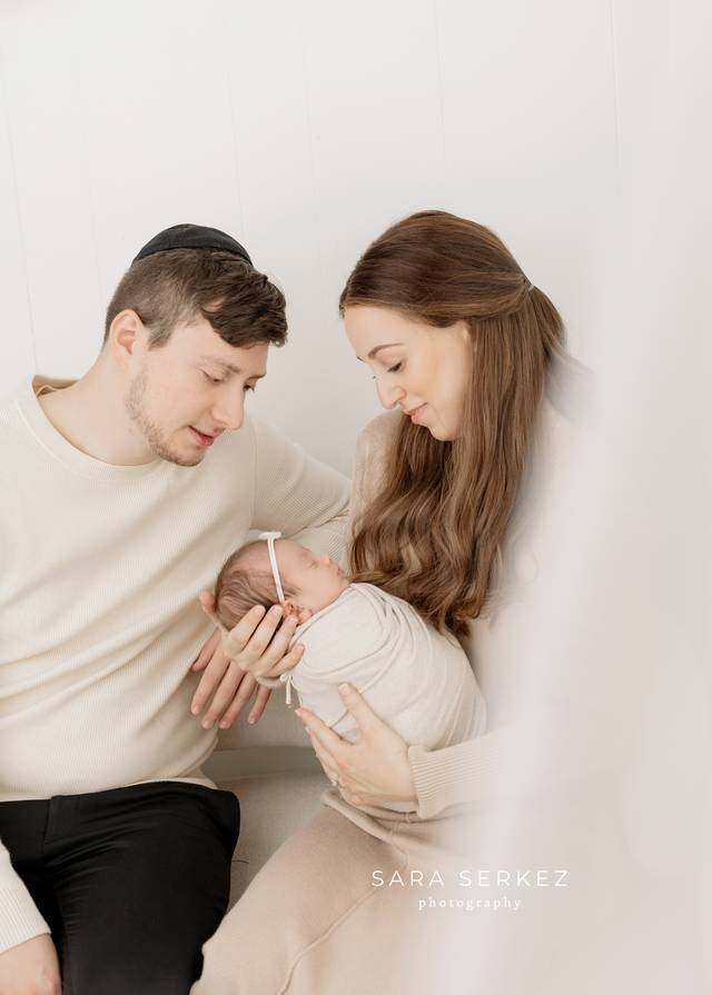 New parents holding their swaddled newborn in a bright white studio.