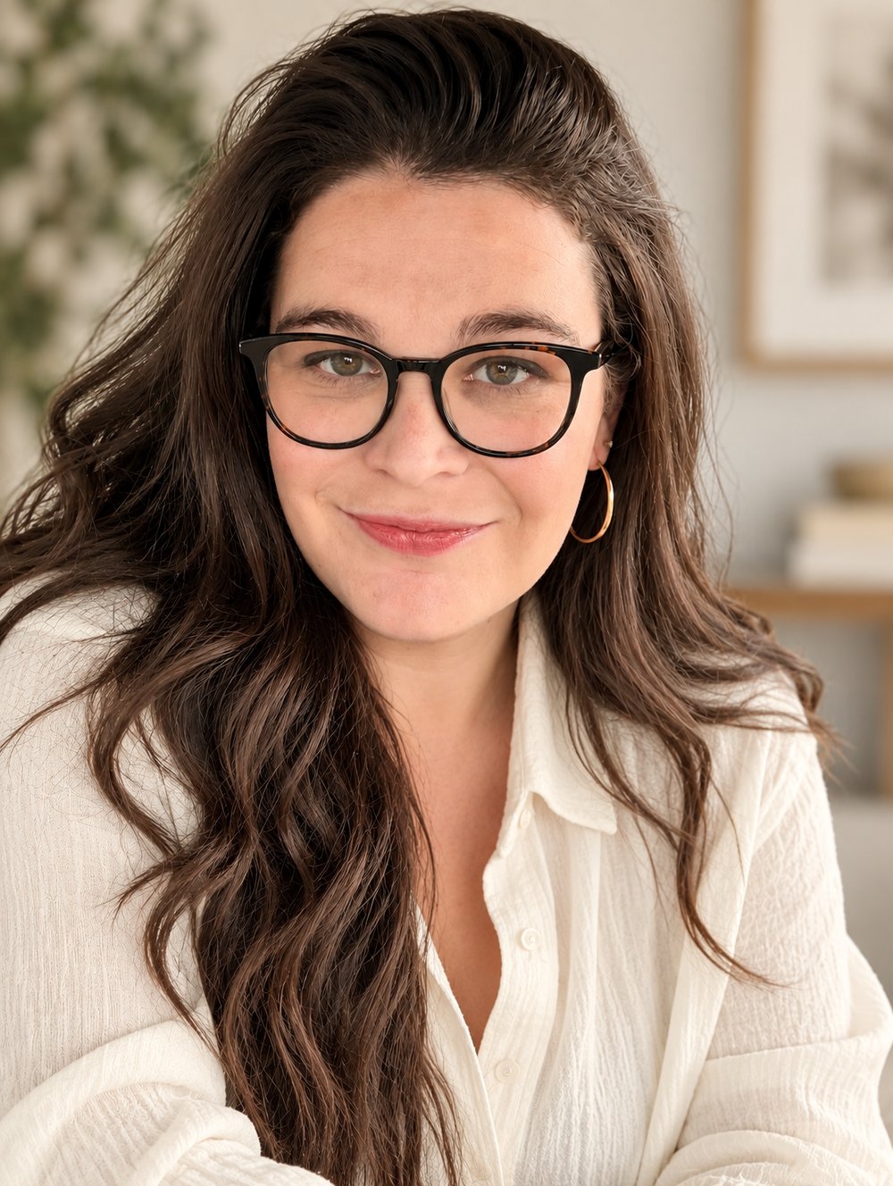 Sara Serkez, dark hair and tortoiseshell glasses, in a cream shirt, smiling at the camera.